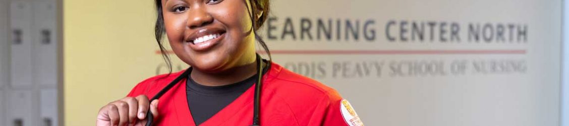 UST nursing student standing in lobby in front of logo smiling