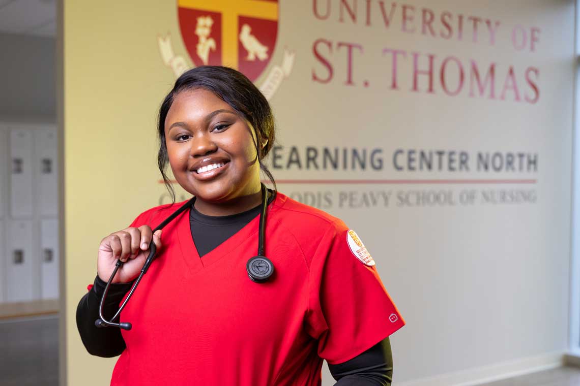 UST nursing student standing in lobby in front of logo smiling